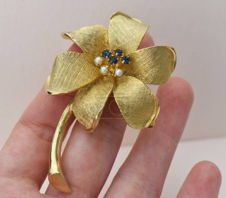 Hand holding a gold flower with a blue and white pearls.