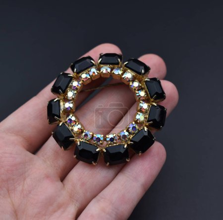 Jewelry brooch in hand on black background. Fashion jewelry.