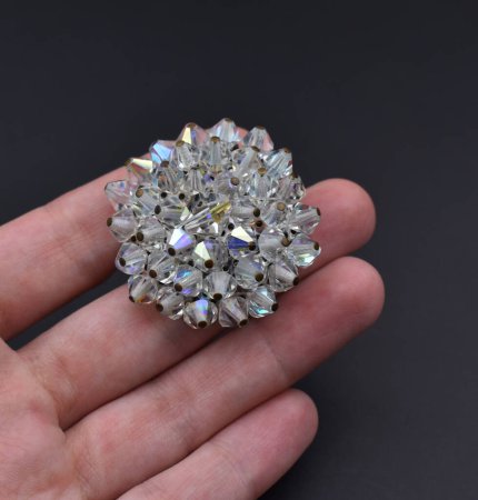 Colorful diamond brooch in hand on black background. Close up.