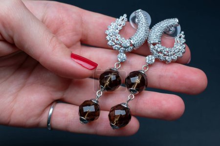 Foto de Pendientes de plata con diamantes de imitación en la mano sobre fondo oscuro - Imagen libre de derechos