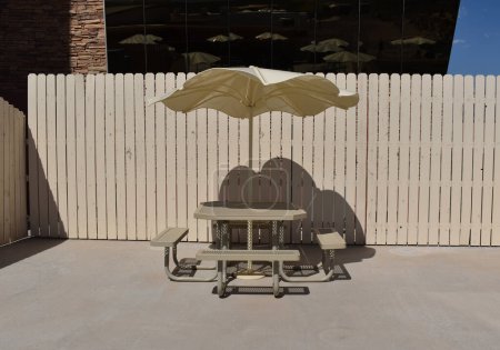 Leere Bänke und ein Tisch unter Sonnenschirm, beiger Sonnenschirm vor dem Hintergrund eines beigen Zauns