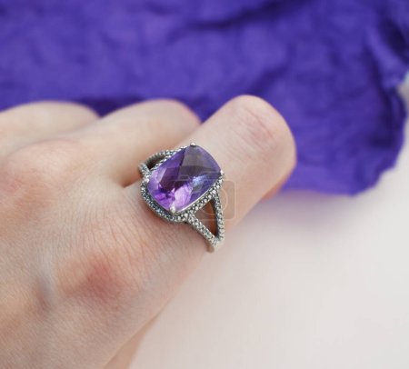 bague à bijoux avec une pierre précieuse violette dans une main féminine