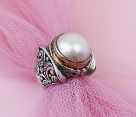 Anillo de joyería con perlas sobre fondo de tela rosa.