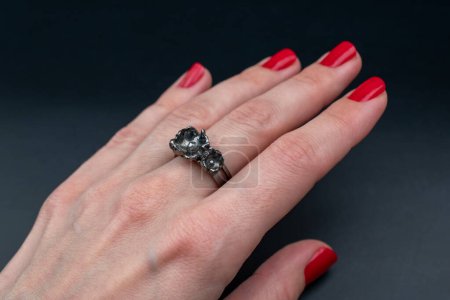 Female hand with red manicure holding ring on black background.