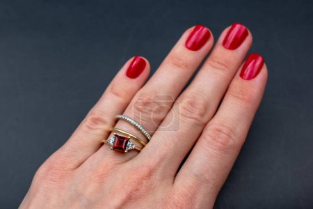 Weibliche Hand mit roter Maniküre, die einen Ring auf schwarzem Hintergrund hält
