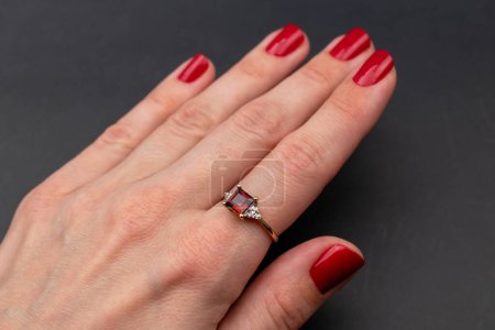 Diamond ring with red nail polish on female hand on black background.