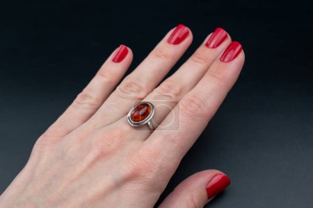 Weibliche Hand mit roter Maniküre, die einen Ring mit rotem Stein hält