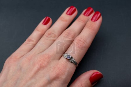 Female hand with red manicure and diamond ring on black background.