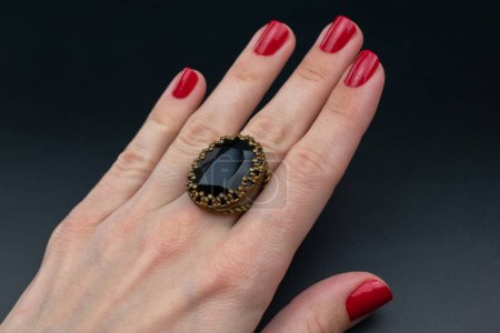 Female hand with red manicure holding black stone ring on black background