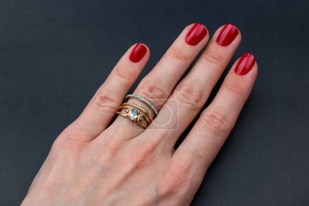 Female hand with red manicure and gold ring on black background.
