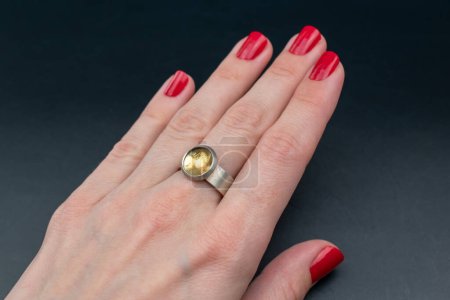 Female hand with red manicure holding gold ring on black background.