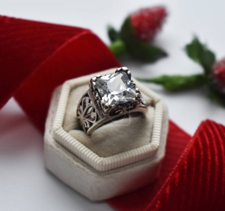Wedding ring with diamond and red ribbon on white background.