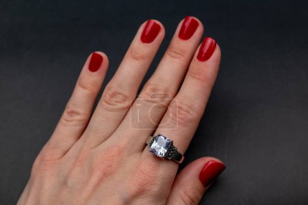 Main féminine avec manucure rouge et bague en diamant sur fond noir.