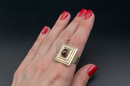 Red manicure with a ring on a black background, close-up