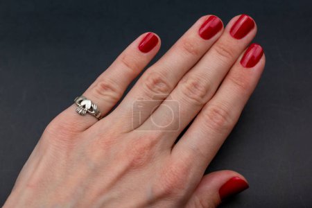 Téléchargez les photos : Main féminine avec manucure rouge tenant une bague sur fond noir. - en image libre de droit