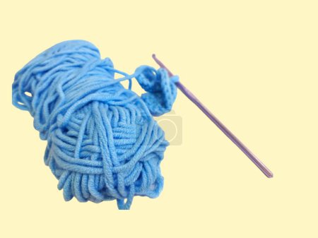 Ball of light blue yarn and crochet hook isolated on yellow background