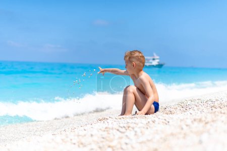 Un garçon joue avec des cailloux sur la belle plage de galets près de l'eau turquoise