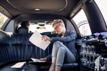 Téléchargez les photos : Femme d'affaires à la recherche de documents en limousine en mouvement - en image libre de droit