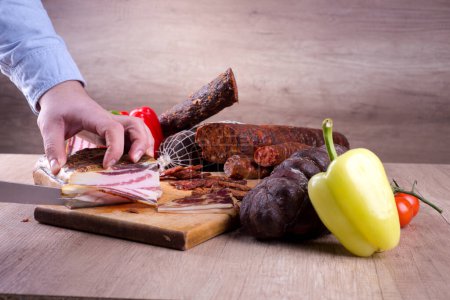 Man is cutting bacon on a wooden board, rustic background