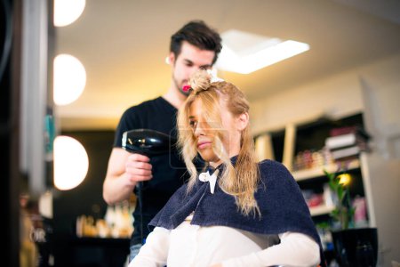 Téléchargez les photos : Jeune fille blonde chez le jeune coiffeur masculin - en image libre de droit