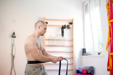 Young man is exercising with physio therapy belts, pulling them on left