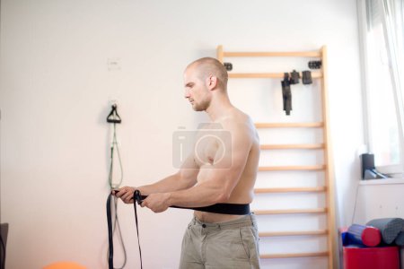 Hombre joven está haciendo ejercicio con cinturones de fisioterapia
