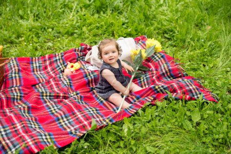 Bébé sur pique-nique, plaçant avec tournesol sur couverture à carreaux