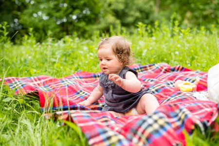 Mignon bébé fille est assis sur une couverture à carreaux dans la nature