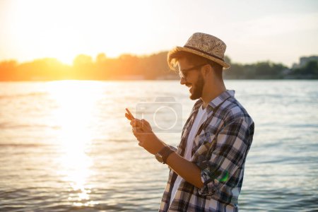 junger Mann benutzt sein Handy am Strand bei Sonnenuntergang