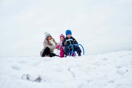Mutter und Kinder beim Rodeln auf schneebedecktem Berg.