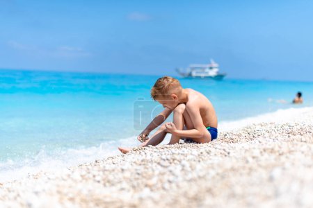 Ein Junge spielt mit Kieselsteinen am schönen Kiesstrand am türkisfarbenen Wasser