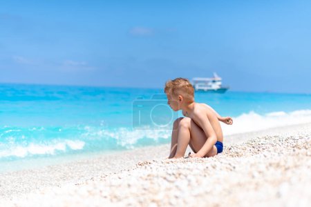 Ein Junge spielt mit Kieselsteinen am schönen Kiesstrand am türkisfarbenen Wasser