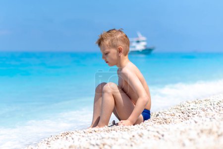 Téléchargez les photos : Un garçon joue sur la belle plage de galets au bord de l'eau turquoise - en image libre de droit
