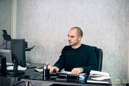 Serious businessman using computer in his office, looking at computer monitor.