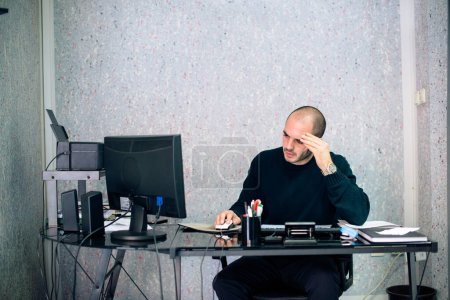 Stressed businessman working in his office, looking at computer monitor and holding head in hands.