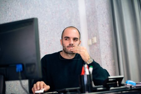 Homme d'affaires caucasien travaillant sur ordinateur, tenant la main sur le menton, regardant concentré.