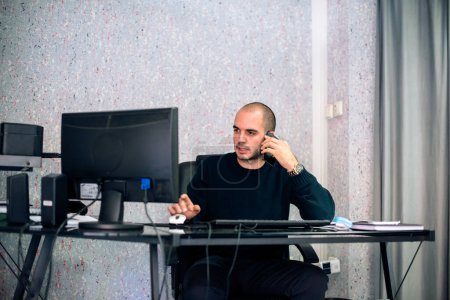 Jeune homme d'affaires caucasien tenant une réunion d'affaires sur téléphone mobile, assis dans son bureau.