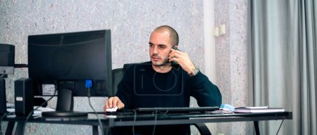 Homme d'affaires multi-tâches parlant sur téléphone mobile et travaillant sur ordinateur, aussi.