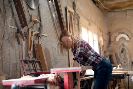 Photo for Young attractive blond woman is working in carpenter workshop - Royalty Free Image