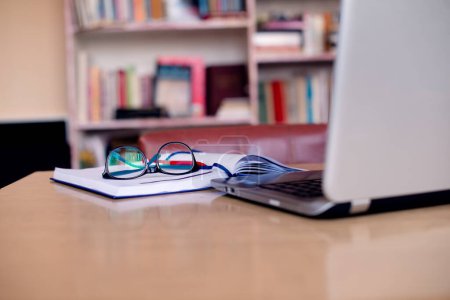 Photo for Laptop, opened notebook and eyeglasses at desk in college library. - Royalty Free Image