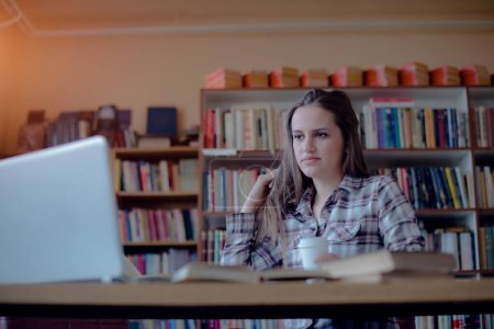 Junge Studentin lernt in Bibliothek am Laptop.