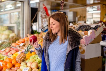 Photo for Portrait of young woman holding red apple at farmer's market. - Royalty Free Image
