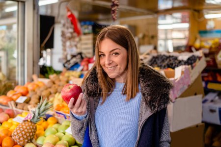 Photo for Smiling pretty woman with fresh apple at farmers's market, looking at camera. - Royalty Free Image