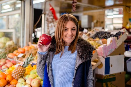 Photo for Caucasian young woman holding apple, smiling and looking at camera. - Royalty Free Image