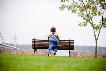 Photo for Young athlete stretching on park bench, rear view. - Royalty Free Image