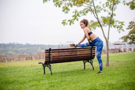 Photo for Sporty woman stretching her legs on park bench. - Royalty Free Image