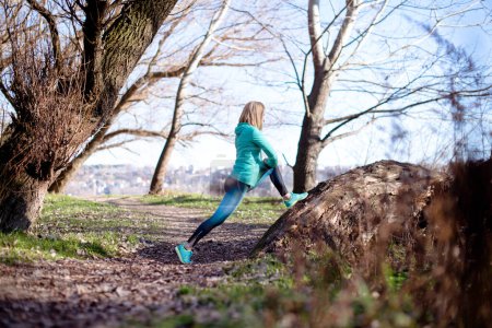 Photo for Sportswoman in nature, stretching her legs. - Royalty Free Image