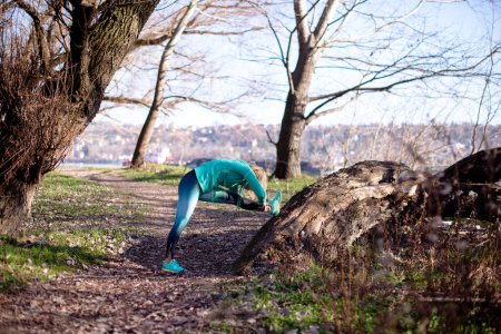Frau streckt ihre Beine auf dem Baum im Park aus, macht Sport in der Natur.