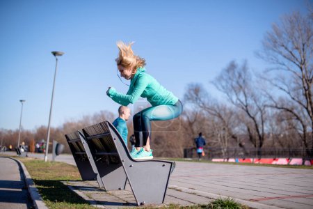 Photo for Healthy female athlete in urban park, exercising on bench. - Royalty Free Image