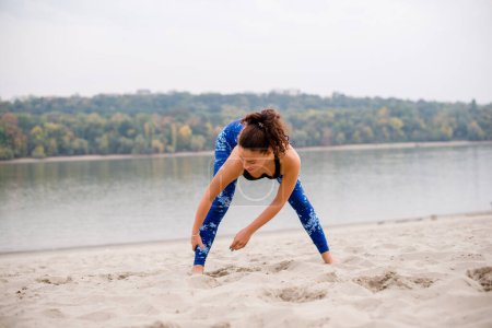 Photo for Woman stretching on sand, preparing for training. - Royalty Free Image